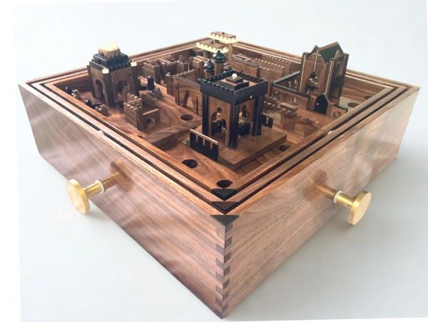 Intricate wooden labyrinth puzzle box with detailed castle-like structures and brass knobs.