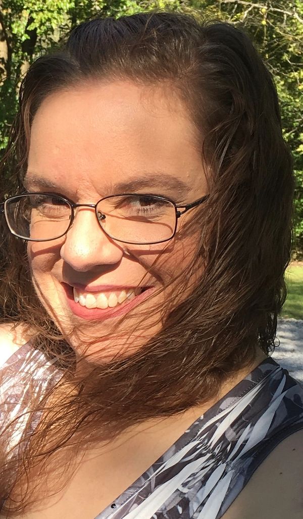Smiling woman with glasses and flowing hair in sunlight.