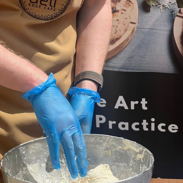 Person wearing blue gloves kneading dough in a metal bowl.