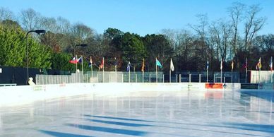 An empty outdoor ice skating rink with flags in the background on a clear day.