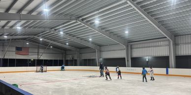 Kids playing ice hockey in an indoor rink with bright overhead lights.