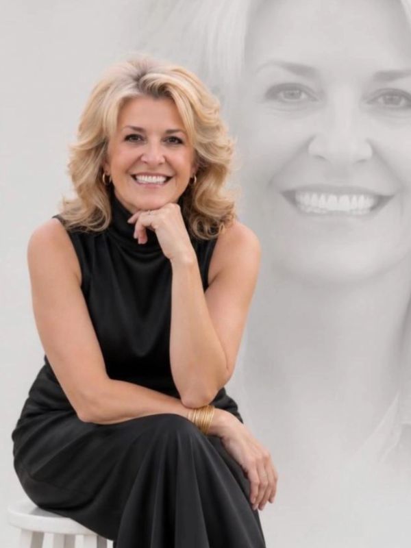 Smiling woman in black dress sitting with a large faded portrait behind her.