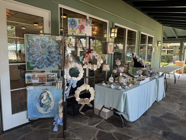 Outdoor craft booth displaying shell wreaths and ocean-themed paintings.