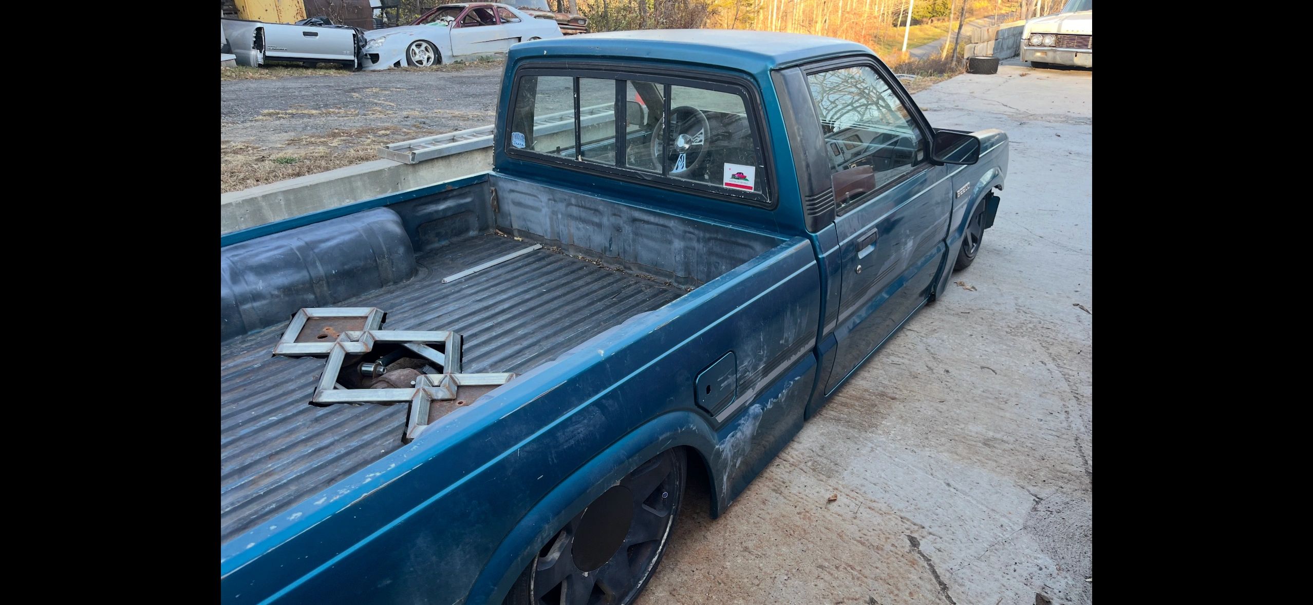 Blue lowered pickup truck with flat bed and large black wheels.
