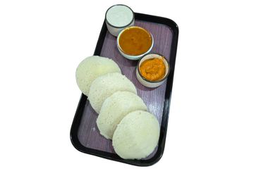 South Indian idlis served with sambar and chutneys on a tray.