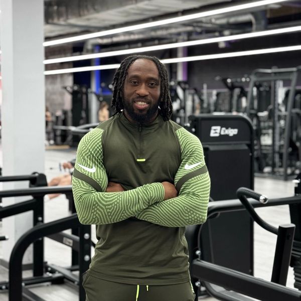 Man in green athletic wear standing with arms crossed in a gym.