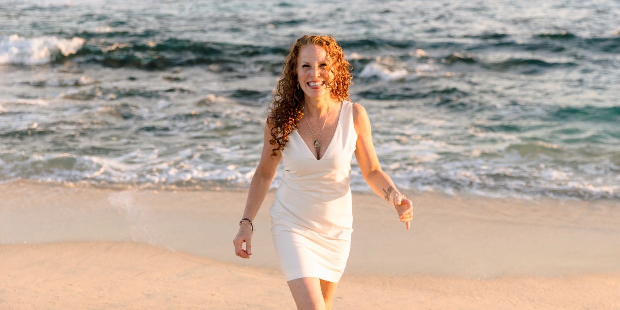 Woman in white dress walking on the beach and smiling.