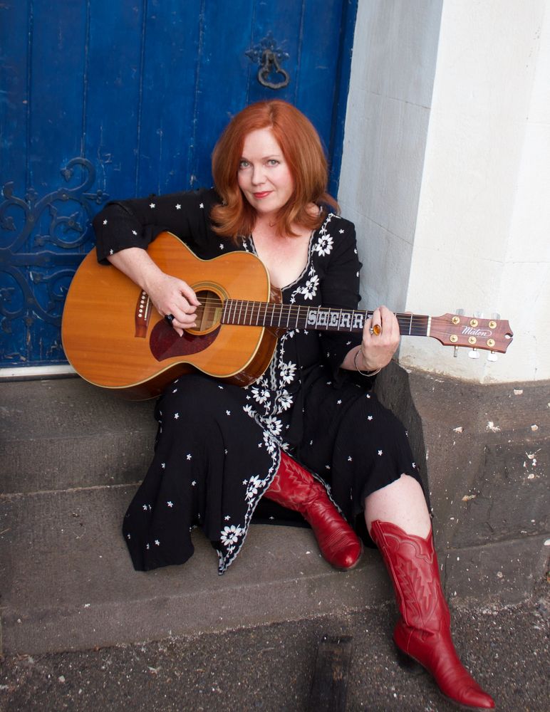 Sherry sitting on a step with guitar in front of a nice blue door