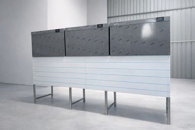 Three sleek, modern industrial machines mounted on a white stand in a minimalistic room.