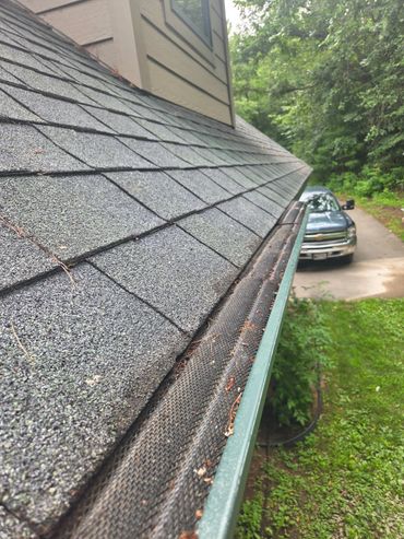 Close-up of a house roof with a gutter guard and a car in the driveway.