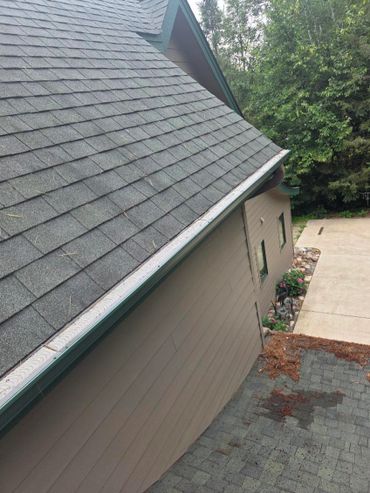 House roof with gray shingles and a clean gutter against a backdrop of trees.