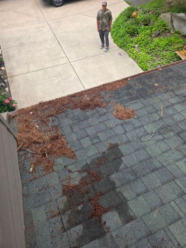 Man stands on driveway near roof with debris and wet patches.