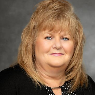 Professional portrait of a middle-aged woman with blonde hair and a black outfit.