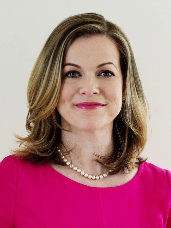 Confident woman with shoulder-length hair, wearing a pink top and pearl necklace.