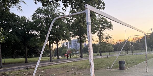 Old, bent soccer goal post in a park at sunset.