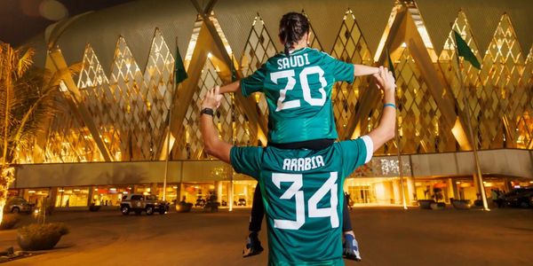 Father and child in Saudi Arabia football jerseys outside a building.