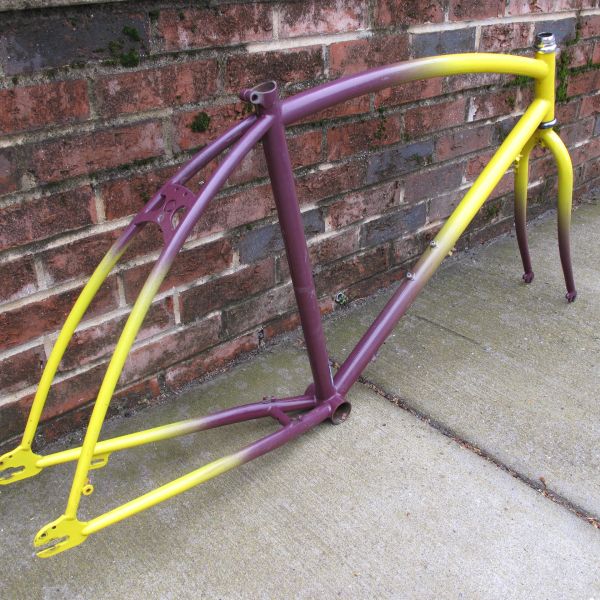 Purple and yellow bicycle frame leaning against a brick wall.