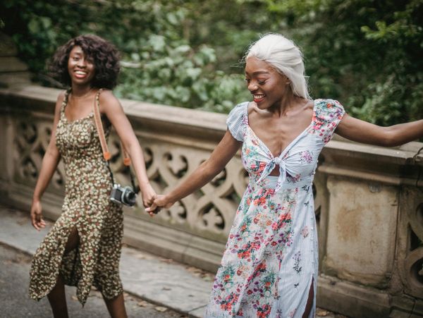 Two Black Women holding hands and smiling on a bridge.