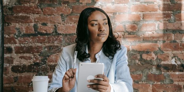 A Black Woman contemplating while holding an electronic pad and pen