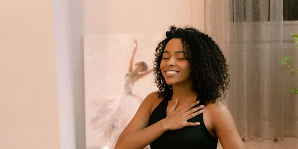 Black Woman with her hand on her chest & stomach, smiling, sitting in front of a laptop cross-legged