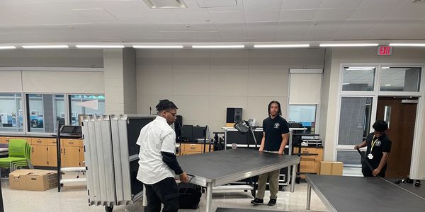 Three people moving tables in a classroom.