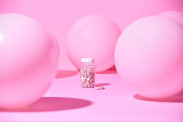 Pink spheres and skincare bottle on pastel background.