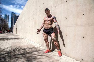 Tattooed bodybuilder posing against wall