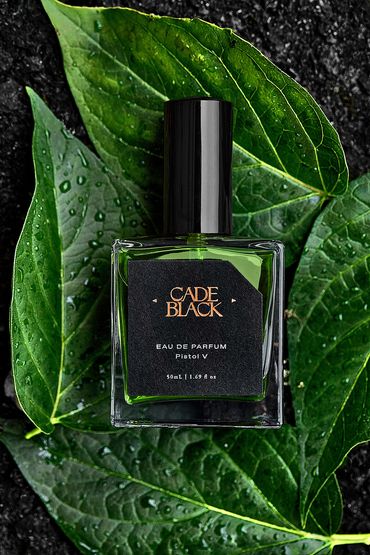 Cade Black perfume bottle on fresh green leaf with water.