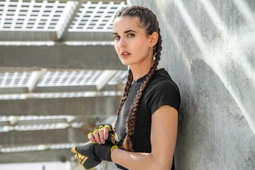 Boxer with braids and gloves leaning against wall.