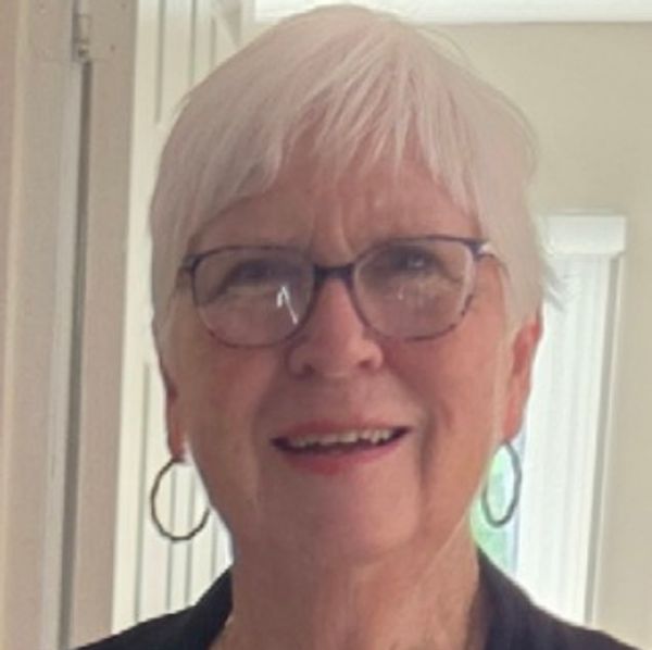 Elderly woman with white hair and glasses smiling.
