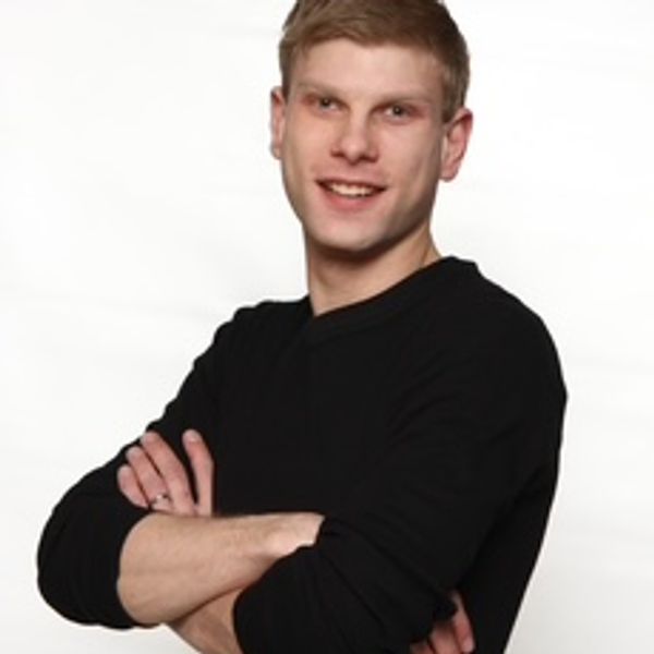 Young man in black shirt smiling with arms crossed.