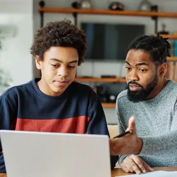 A man teaching a teenage boy using a laptop at home.