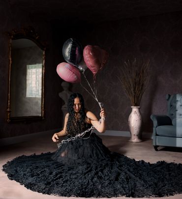 Portrait of a young woman in an elegant black dress sitting in her living room holding balloons