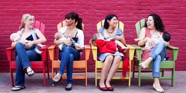 Four women (white, black, native, latino) breastfeeding in chairs with a brick wall behind them. 