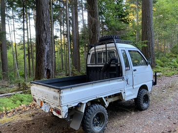 A small white off-road truck parked on a forest trail.