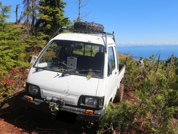 Small white off-road vehicle parked on a rugged trail in a forested area.