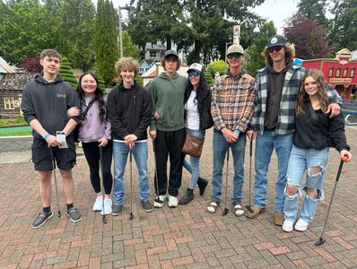Group of young people posing with mini golf clubs outdoors.