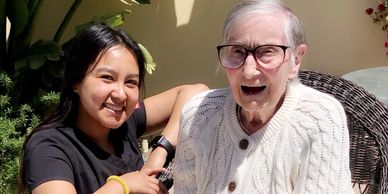 A young woman smiling next to an elderly woman in a cozy outdoor setting.