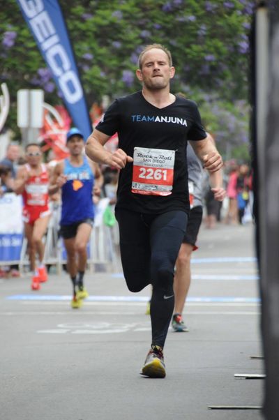 Runner in black outfit nearing the finish line in a race.