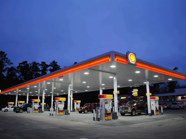A well-lit Shell gas station at dusk with several vehicles refueling.