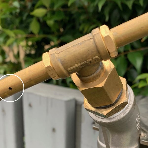 Close-up of a brass pipe joint with a small hole in the pipe.