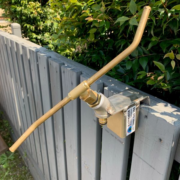 A brass water spigot on a gray wooden fence.
