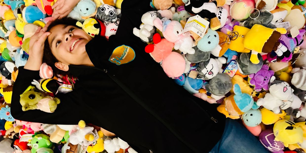 A young person lying happily on a colorful pile of plush toys.