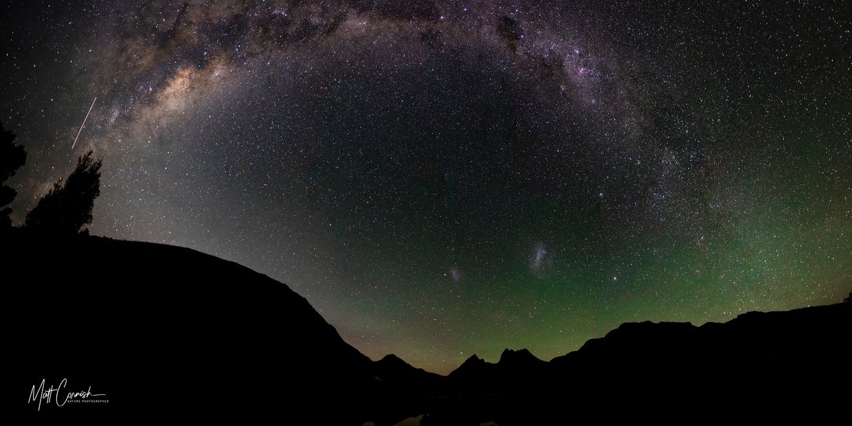 Milky Way arching over a mountain silhouette at night.