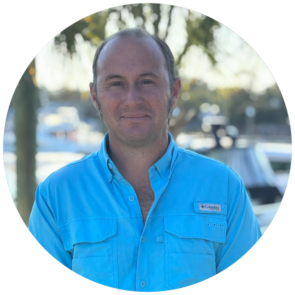 Man in a light blue Columbia shirt smiling outdoors near water.