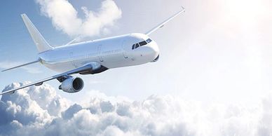 White commercial airplane flying above fluffy clouds in sunny sky.