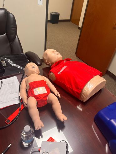 Two CPR training mannequins, adult and infant, on a table in an office.