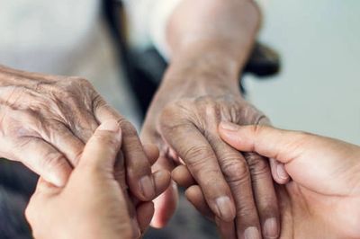 Young hands gently holding elderly hands in a comforting gesture.