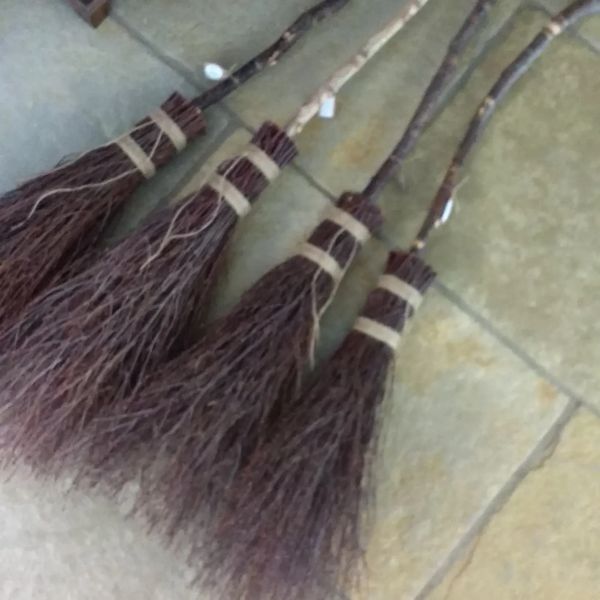 Four rustic handmade twig brooms with wooden handles on the floor.