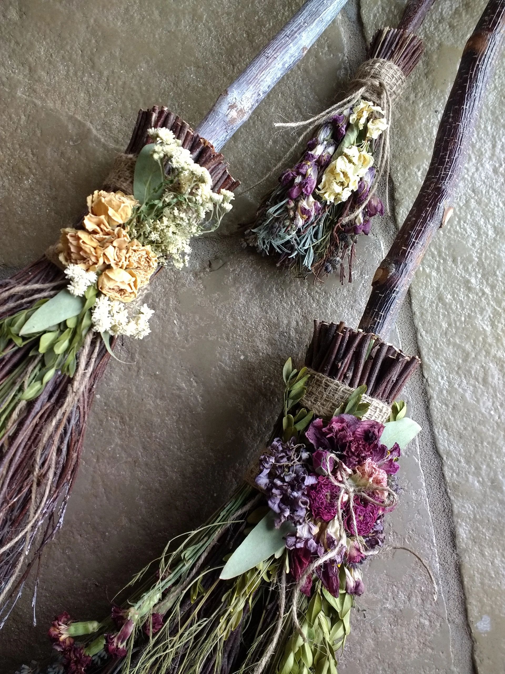 Handcrafted twig brooms adorned with dried flowers and burlap wraps.